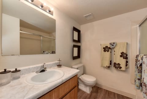 Model bathroom with towels hung on the racks and on the sliding shower doors.  Hardwood inspired flooring and nice lighting.